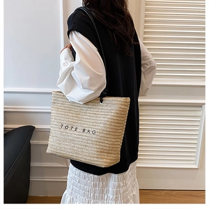 Detailed close-up of beige straw tote bag with black leather straps and Tote Bag text