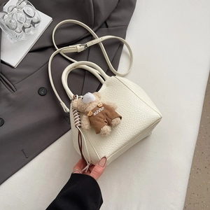 Détail d'un mini sac seau en cuir blanc avec un pendentif ours en peluche sur un bureau
