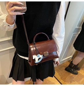 Detail of a dark brown leather tote bag with a decorative horse charm and shoulder strap