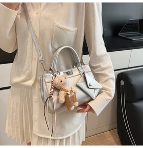 Detail of silver metallic handbag with plush bear charm and mini envelope accessory
