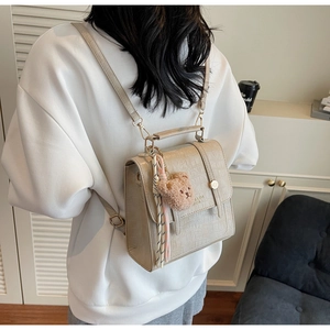 Detail of beige faux crocodile leather backpack with plush bear and ribbon accessory