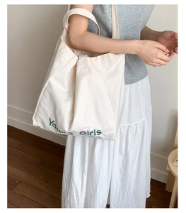 Detail of white canvas tote bag with green Young girls embroidery and natural texture