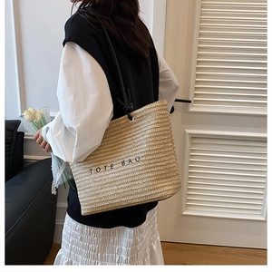 Detail of woven tote bag with TOTE BAG embroidery and black shoulder strap on model