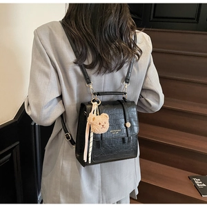 Detail view of black crocodile pattern backpack with bear charm and silk ribbon on model
