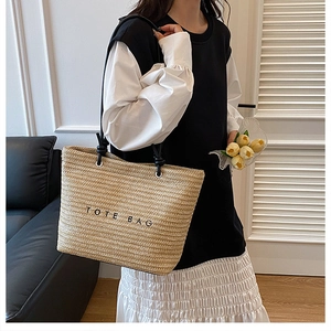Detail shot of a beige straw tote bag with black TOTE BAG embroidery and slim straps