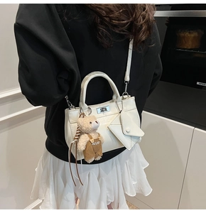 Detail of white glossy faux leather handbag with cute teddy bear and mini pouch charms