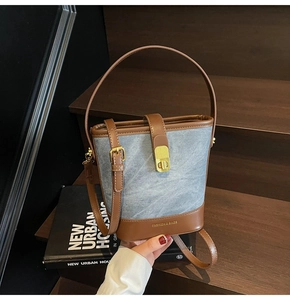 Detail of denim bucket bag with brown trim, golden hardware and fashion lettering