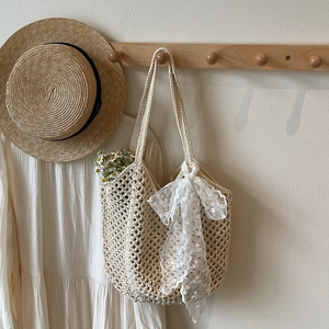 Détail de la texture d'un sac tissé main beige orné d'un grand nœud en dentelle blanche