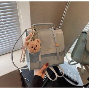 Detail of light blue croc-embossed handbag with gold metal handle and teddy bear charm
