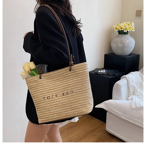 Detailed texture of woven straw tote bag featuring black embroidered lettering and leather straps