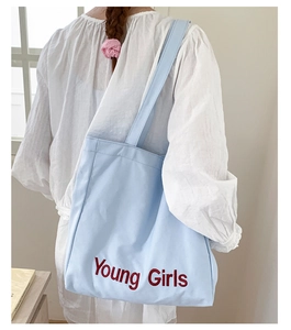 Close-up of a blue canvas shoulder bag with red Young Girls lettering on a model