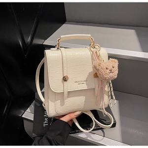 Detail of cream white faux crocodile leather bag with gold logo and plush bear charm