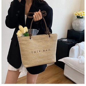 Close-up of woven straw tote bag with brown rope handles and black embroidered TOTE BAG text