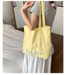 Detailed view of yellow canvas tote bag with Young Girls blue embroidery and sturdy strap