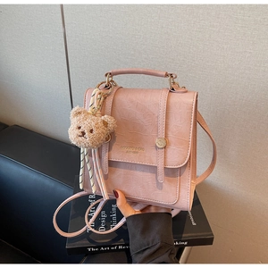 Detail of pink croc-embossed crossbody bag with a plush bear charm and adjustable strap