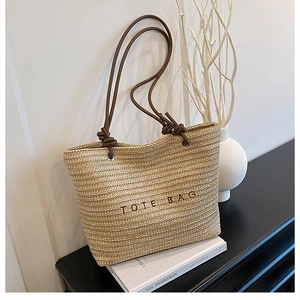 Macro view of woven beige straw tote bag with brown embroidered lettering and leather straps