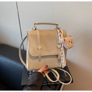 Detail of khaki crocodile-embossed crossbody bag with plush bear charm and tassels