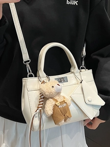 Cream white handbag with plush bear pendant and detachable shoulder strap on casual outfit