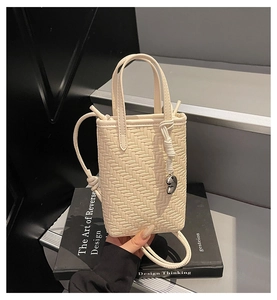 Detail view of cream woven crossbody bag with a silver heart charm and knotted strap