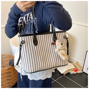 Detail showing a striped tote bag with black leather straps and a plush dog charm
