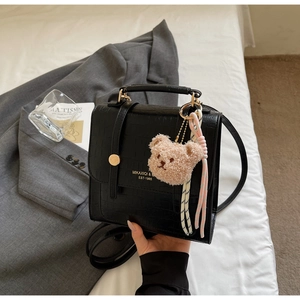 Detail of black crocodile texture handbag with gold buckle and plush bear charm