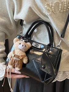Glossy black handbag with teddy bear charm and silver twist lock in model's hand