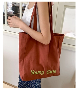 Detailed close-up of brick red canvas tote bag with Young Girls green embroidery