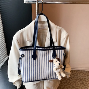 Detail of blue striped tote bag with leather trim and cute plush dog pendant accessory