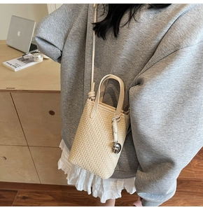 Detail view of cream woven crossbody bag with metallic pendant on a model