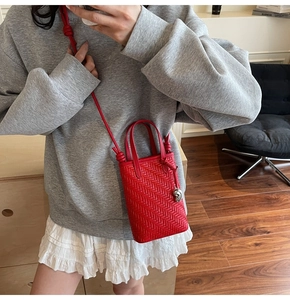 Detail of red woven mini tote bag with crossbody strap and silver charm on gray outfit