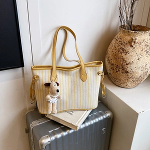 Detail of yellow striped canvas tote bag with leather handle and dog plush charm