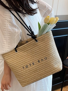 Large beige woven tote bag with TOTE BAG print and black handles for summer beach use
