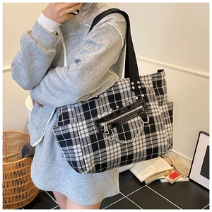 Close-up of checkerboard tote bag featuring metal rivets, decorative chains and zip pockets