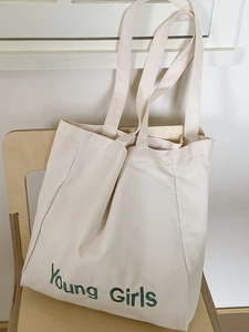 Minimalist cream canvas tote bag with green Young Girls print on a wooden chair