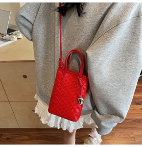 Detail of red woven mini crossbody bag with a silver heart charm on casual background