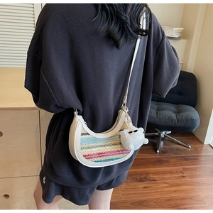 Rear view of a rainbow woven crossbody dumpling bag with white plush charm on a model