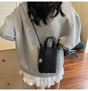 Detail of black woven mini crossbody bag with knot shoulder strap and silver metal charm