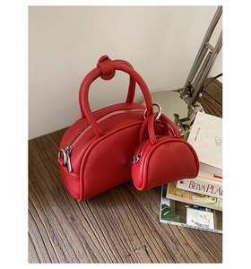 Détail du sac bowling en cuir rouge à motif litchi et mini breloque sur bureau en bois
