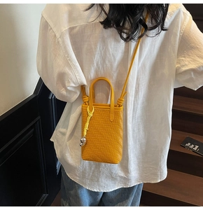 Detail of yellow woven leather crossbody phone bag with silver pendant and shoulder strap