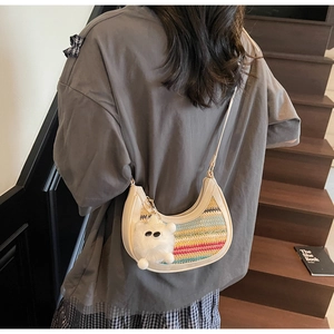 Detail of a rainbow woven crescent bag with a white plush bear charm and slim strap