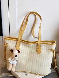 Striped canvas tote bag with yellow leather handles and a plush dog charm on a suitcase