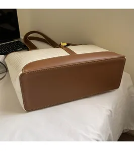 Close-up of white crocodile embossed leather tote bag with brown trim and gold metal lock