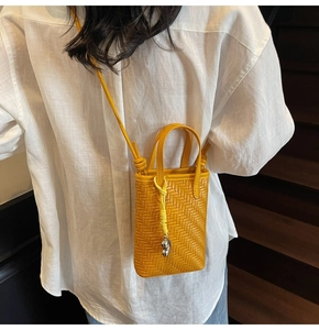Detail of bright yellow woven crossbody phone bag featuring a silver metal charm