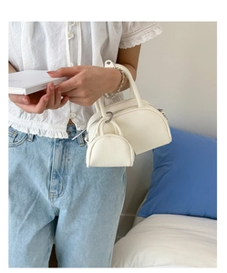 Détail du sac Boston blanc crème avec texture grainée et mini breloque sur la poignée