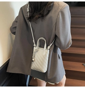 Detail of silver woven mini tote bag with knotted shoulder strap worn with grey suit