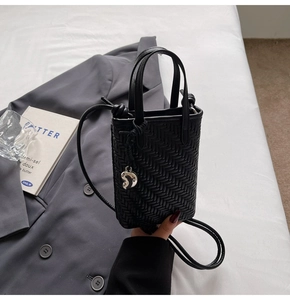 Detail of black woven mini crossbody bag with herringbone texture and silver pendant