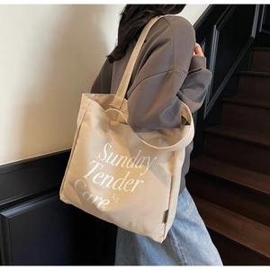 Detalle del bolso tote de lona beige con letras Sunday Tender Care y correa para el hombro