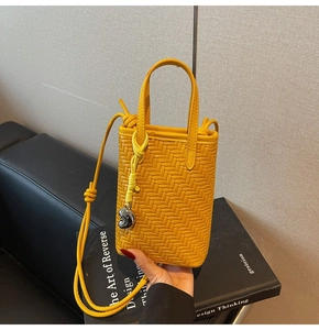 Close-up of yellow woven mini tote bag with heart charm and shoulder strap