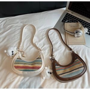 Detail of rainbow woven crossbody dumpling bags with plush lamb charms on white fabric