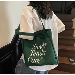 Detalle del bolso tote de lona verde oscuro con letras blancas en escalera de madera